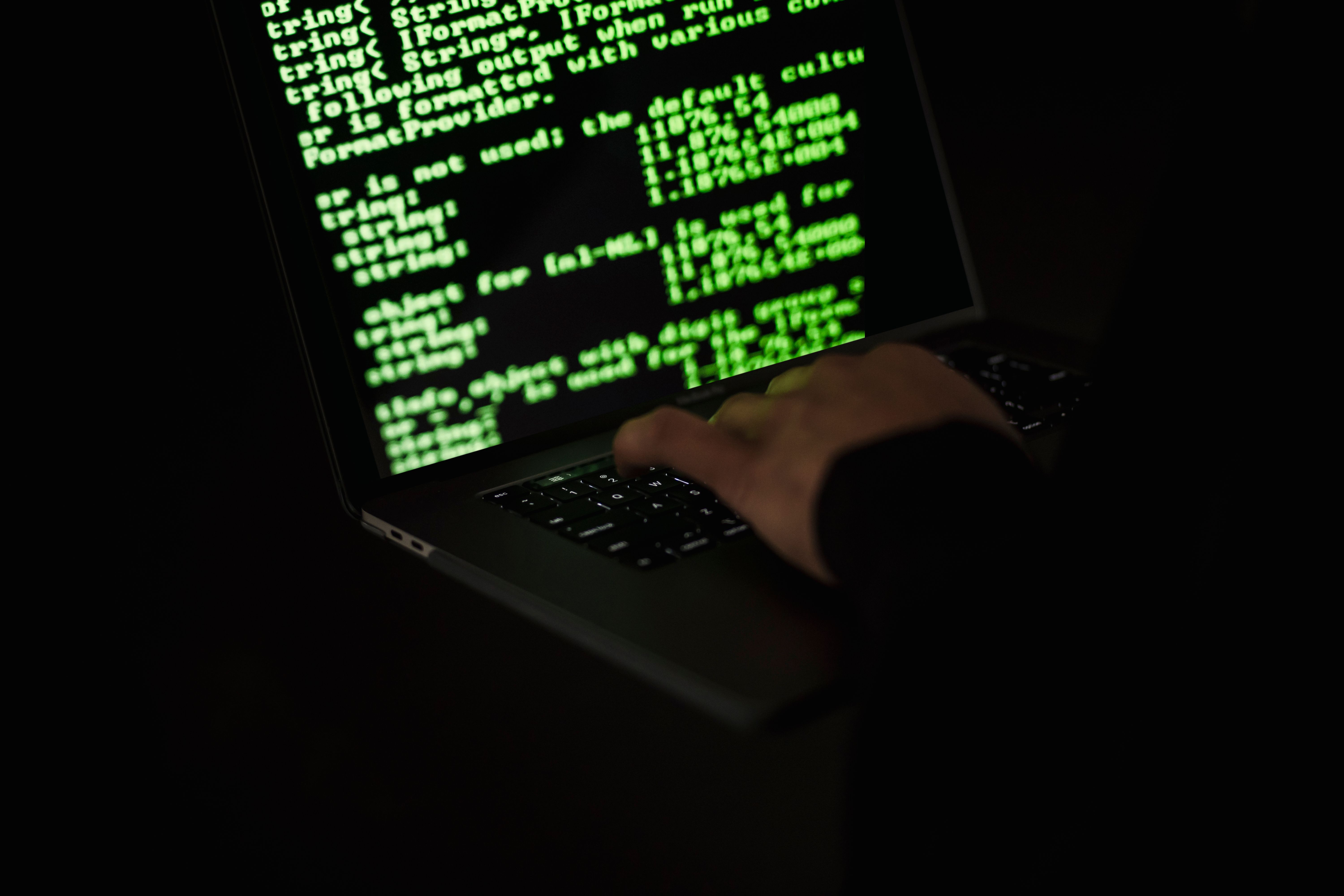 An anonymous hacker typing code on a laptop in darkness, illustrating attempts to obscure digital activity.